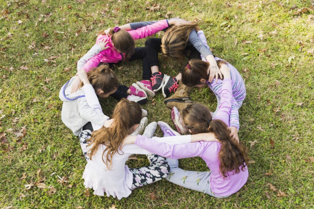 Che cosa sono le non-cognitive skills? group girls sitting together huddle green grass 678908d8dbbc5 bambine abbraccio